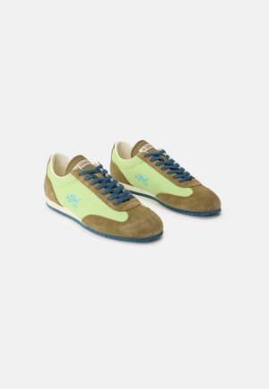 Paire de baskets en daim vert et marron avec des lacets bleus et une doublure intérieure blanche, placées côte à côte sur un fond gris.