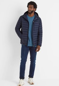 Navy puffer jacket with a hood, zip closure, and stitched paneling. Worn over a blue sweatshirt, paired with dark jeans and white sneakers.