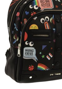 Sac à dos synthétique noir orné d'imprimés graphiques colorés, incluant des emojis et des phrases. Une poche zippée à l'avant et des éléments décoratifs métalliques sont présents.