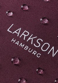 Tessuto marrone con texture in rilievo, caratterizzato da gocce d'acqua e dal testo impresso "LARKSON HAMBURG" in bianco, che mette in evidenza durevolezza e design.