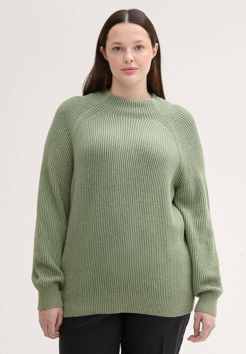 Grüner gerippter Pullover mit langen Ärmeln und rundem Halsausschnitt, mit lockerer Passform und strukturiertem Stoff. Getragen über schwarzen Hosen.