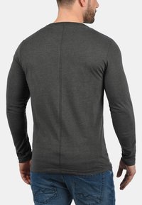 Langermet skjorte i mørkegrå bomull, med rund hals, slim fit, og vertikal sømdetalj på baksiden. Kombinert med blå jeans.