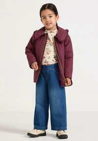 Maroon insulated jacket with ruffled collar, gold zipper. White floral-patterned top, blue wide-leg jeans, beige boots. Simple design and textures.