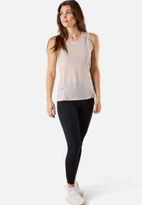 Light beige sleeveless top with a smooth texture, paired with black leggings and white athletic shoes. Simple, fitted design with minimal detailing.