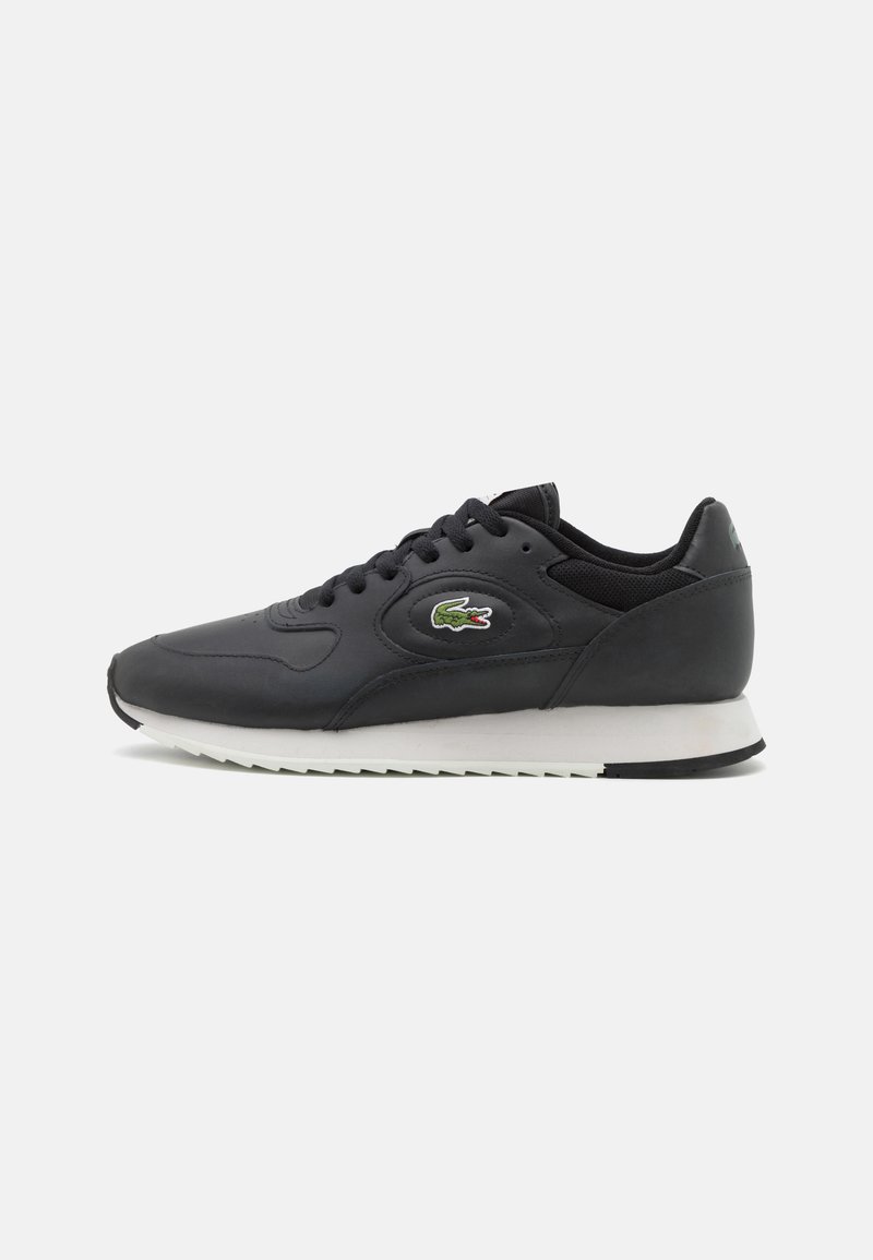 Chaussure de sport en cuir noir avec semelle intermédiaire blanche, accents texturés, fermeture à lacets et un petit logo coloré sur le côté.
