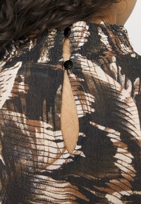 Tecido com padrões em preto e castanho, com um recorte para o pescoço e dois botões escuros. O tecido texturizado apresenta um design semelhante a folhas.