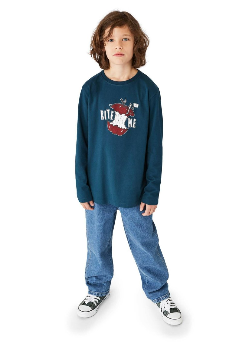 Langärmliges navy-blaues Shirt mit bedrucktem roten Apfelmotiv und dem Text "BITE ME", kombiniert mit hellblauen Jeans und schwarz-weißen Sneakern.