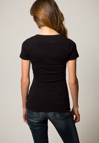 Schwarzes kurzärmeliges T-Shirt mit tailliertem Schnitt, glatter Textur und rundem Halsausschnitt. Getragen mit dunkel gewaschenen Jeans mit Gesäßtaschen.