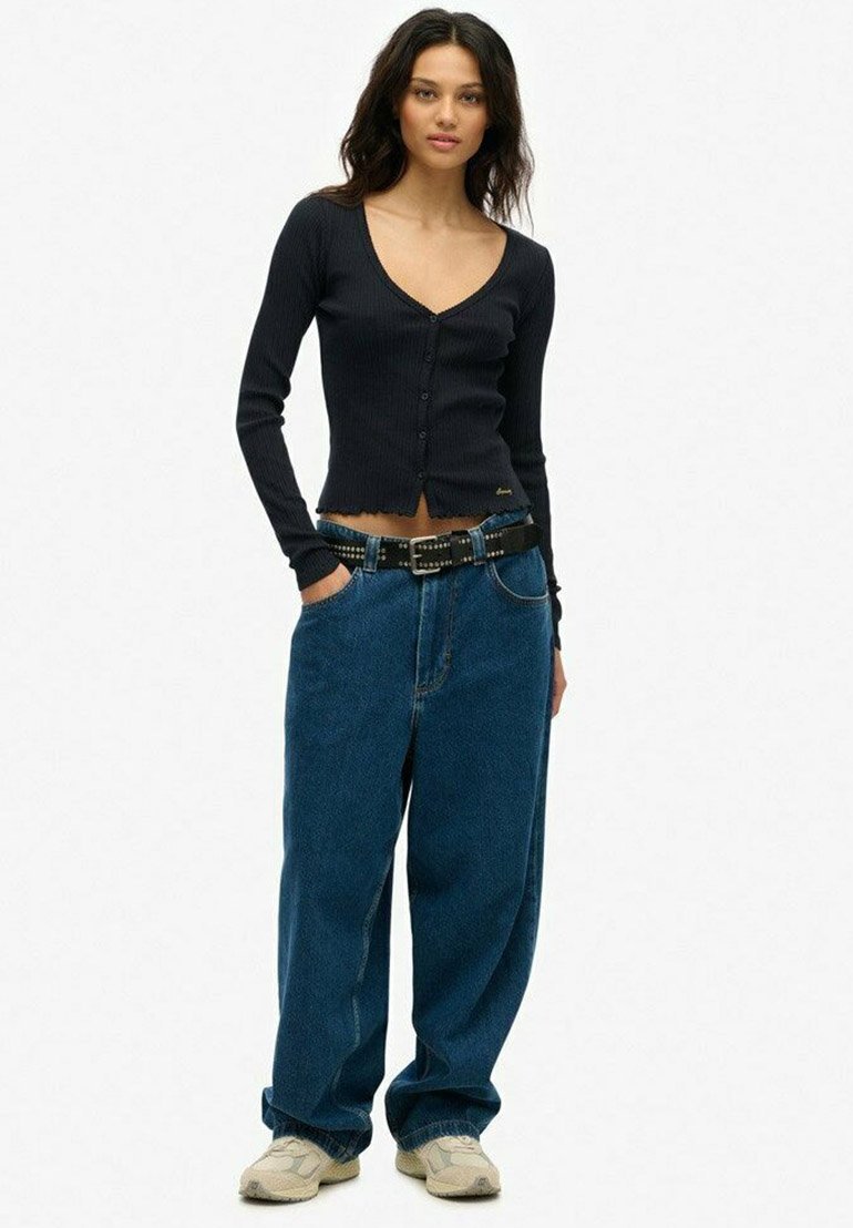 Sort ribbet langærmet cardigan med V-hals og frontknapper, parret med højhæjede, blå baggy jeans og et sort naglet bælte.