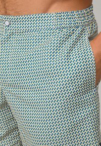Gemusterte Shorts mit einem geometrischen Design in Blau und Gelb auf einem hellen Hintergrund. Das Material ist leicht und hat eine glatte Textur.