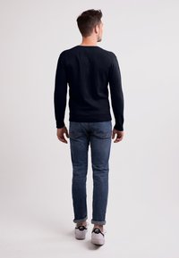 Marinblå stickad tröja med långa ärmar och rundad hals, matchad med ljusblå jeans och vita sneakers. Enkel, strukturerad design, sedd bakifrån.