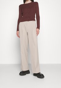 Bordeauxrood geribd vest met ronde hals en bruine knopen, gecombineerd met beige broek met wijde pijpen en zwarte chunky plateauzolen.