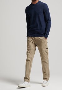 Marineblauer Strickpullover mit Rundhalsausschnitt, kombiniert mit beigen Cargo-Hosen mit mehreren Taschen und hellbraunen Sneakers.