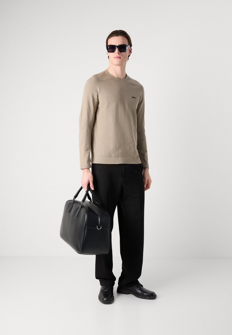 Camisa de manga larga beige con tela texturizada, pantalones negros y bolso de cuero negro brillante. Los accesorios incluyen gafas de sol negras de gran tamaño y zapatos.