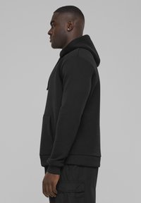 Čierna mikina s kapucňou a klokankou, vyrobená z mäkkej tkaniny. Obsahuje rebrované manžety a lem, pričom zobrazuje priliehavý strih.