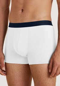 Boxer shorts bianchi in cotone con una vita elastica blu navy che presenta un marchio in rilievo. Il design è aderente e presenta una texture liscia.