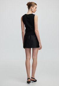 Top negro sin mangas y falda corta tipo A negra. Texturas suaves con un diseño ajustado y una cintura sutil. Unos sencillos tacones negros completan el look.