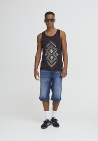 Black tank top with white geometric pattern, blue denim shorts, white socks, and black sneakers, accessorized with sunglasses.