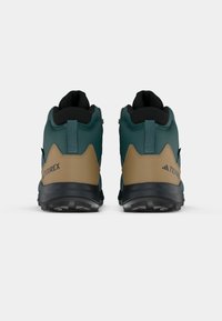 Botas de caminhada para homens com um cabedal em verde-azulado escuro, detalhes em bege, uma gola texturizada preta e uma sola preta robusta com padrões de tração.
