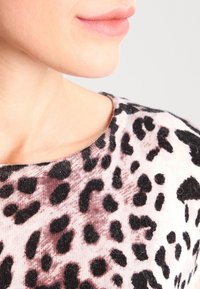 Zbliżenie dolnej części twarzy i szyi osoby noszącej miękki sweter w różowo-czarny wzór w panterkę.