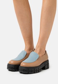 Chaussures slip-on en cuir marron avec un accent texturé bleu clair, semelles plateformes noires épaisses et design à bout rond.