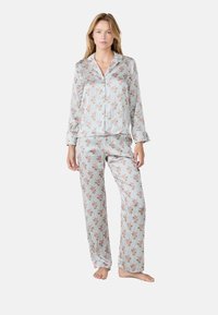 Pyjama set met bloemenpatroon, bestaande uit een knoopshirt en lange broek. De stof heeft verticale strepen in lichte kleuren met roze bloesems.
