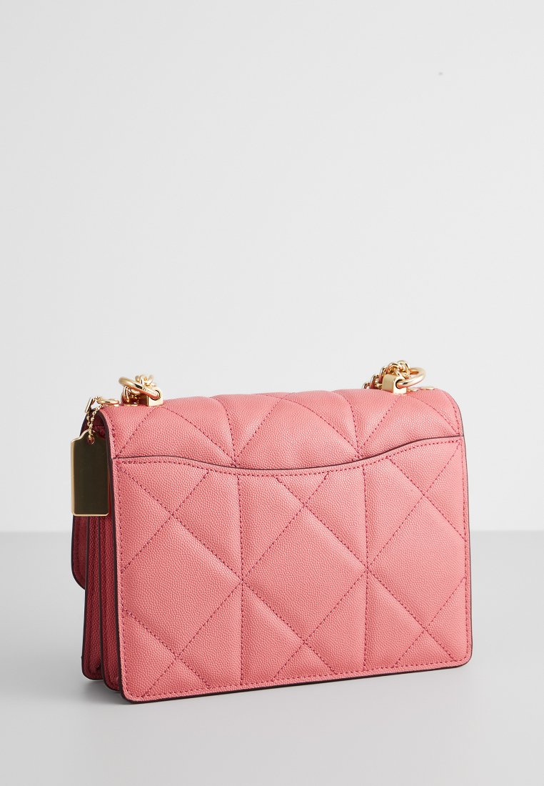 Bolso de mano de cuero acolchado rosa con una correa de cadena, que presenta un sutil patrón en relieve y una forma rectangular. Incluye un detalle en tono dorado.