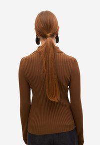 Suéter largo de manga larga ribeteado en marrón con cuello tipo polo y diseño ajustado. Presenta una textura suave y una vista posterior con cabello lacio.