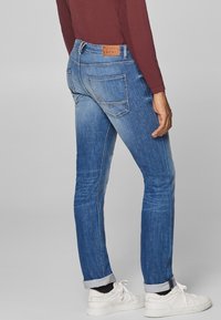 Slim-fit siniset farkut, joissa on haalistunut ilme, kaksi takataskua ja brändätty nahkapatchi vyötäröllä. Yhdistetty valkoisiin tennareihin.