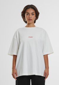Tricou supradimensionat alb din bumbac, cu guler rotund și mâneci scurte, având un text brodat roșu care spune "Interzis."