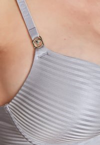Reggiseno grigio con strisce a trama e una finitura liscia e lucida. Presenta un dettaglio in metallo argentato sulla tracolla e un design senza cuciture.