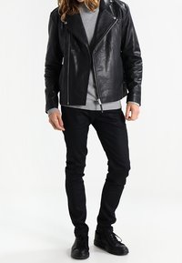 Schwarze Bikerjacke aus Leder mit asymmetrischem Reißverschluss, grauer Rundhalspullover, schwarze eng anliegende Jeans und schwarze Sneakers. Glatte Textur und taillierte Form.