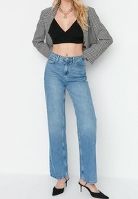 Jeans de mezclilla de talle alto en un tono azul claro con corte relajado, combinados con un top corto negro y una blazer a cuadros. Tacones negros de punta completan el look.