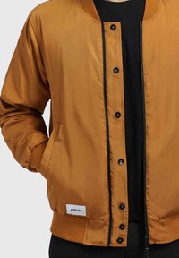 Bronzen bomberjack van glanzend polyester, met een ribgebreide kraag en manchetten, voorzien van een rits en drukknoopsluitingen, en een logotag.