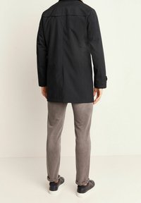 Svart jacka med rak skärning, långa ärmar och en bakre slits, tillsammans med gråa smala byxor och mörka sneakers. Mjuk tygstruktur.