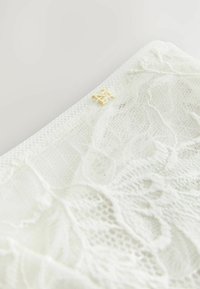 Hvid spidsedug med blomstermønster, der har en gulddetalje. Blød tekstur og delikat design, der viser intrikate sting.