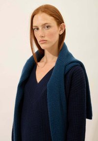 Teksturowany granatowy sweter z głębokim dekoltem w serek i ciemnoniebieskim szalem. Materiały wydają się być dziane, co dodaje głębi całkowitemu wzornictwu.