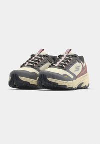 Paire de baskets de randonnée basses beige, gris et marron avec semelles noires et fermeture à lacets sur fond blanc uni.