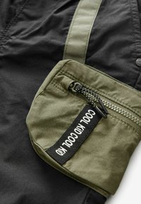Green fabric pouch with zipper and black strap featuring white text "COOL KID" on black clothing background.