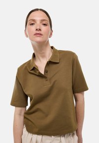 Polo à manches courtes de couleur kaki en tissu texturé, avec un col et une patte de boutonnage à trois boutons, offrant une coupe décontractée.