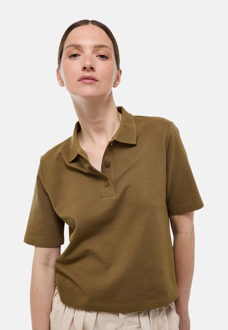 Polo à manches courtes de couleur kaki en tissu texturé, avec un col et une patte de boutonnage à trois boutons, offrant une coupe décontractée.