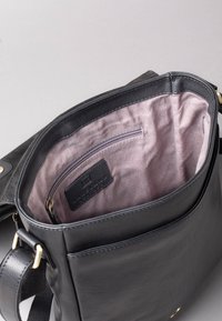 Black leather handbag interior with soft mauve lining, zip pocket, and brand tag. Features top opening and an adjustable strap.