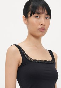 Débardeur noir avec un décolleté carré et des bordures en dentelle délicate. Confectionné en tissu doux, il dispose de bretelles étroites et d'une coupe ajustée.