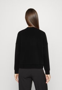 Sudadera negra de corte holgado, con puños y dobladillo acanalados, textura suave y cuello redondo, vista desde atrás.