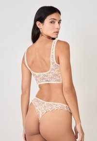 Bralette in pizzo floreale e thong abbinati, caratterizzati da un design giallo pallido, bordi ondulati e una trama trasparente con accenti rosa e verdi.