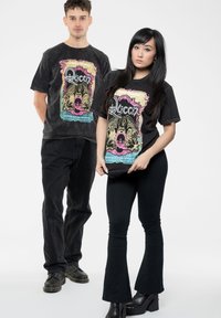 Black graphic t-shirts featuring a colorful "Queen" design with eagle and crown illustrations, worn with black pants and chunky shoes.