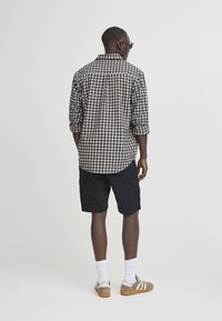 Geruit overhemd in beige en marineblauw, zwarte cargoshorts, witte sokken en bruine sneakers. Zichtbare stiksels en details van zakken.
