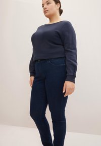 Sudadera de color azul marino con cuello redondo y mangas largas, combinada con jeans de un azul oscuro que tienen un corte clásico y bolsillos frontales.