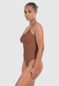 Body senza maniche marrone con una texture liscia e elastica e un design a gamba alta, che mostra accenti in tonalità della pelle.