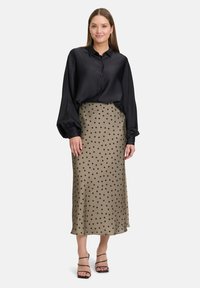 Blusa di raso nera con chiusura a bottoni, maniche lunghe a sbuffo; gonna midi beige con pois; abbinata a sandali neri con cinturini.